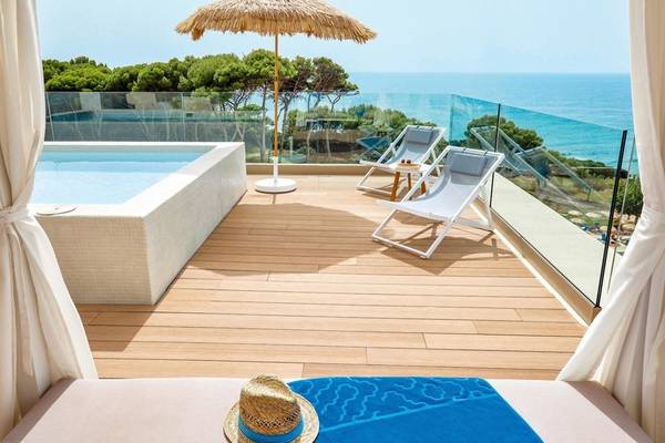 Terrasse mit Meerblick im Victoria Menorca Hotel, mit Jacuzzi, Sonnenliegen und Sonnenschirm.