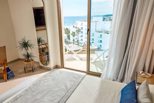 Schlafzimmer mit Meerblick im Victoria Menorca Hotel, mit Bett, Balkon, Pflanzen und Ausblick auf das Meer.
