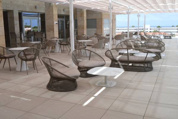 Hotelterrasse mit Tischen und Stühlen unter einem Sonnendach im Freien.