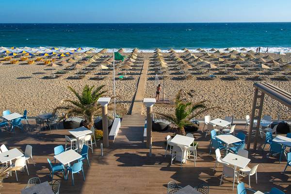 Aussicht auf die Terrasse des Odyssia Beach Hotels mit Tischen, Stühlen und Sonnenschirmen am Strand