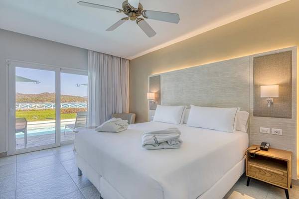 Schlafzimmer im Senator Puerto Plata Spa Resort mit einem Bett, Decken, Kissen und einem offenen Balkon.