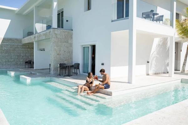 Paar vor einer weißen Villa am Pool mit glasgeländer und terrassenmöbeln