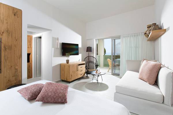 Innenansicht des Schlafzimmers im Agapi Beach Resort mit Doppelbett, Sofa und Fernseher.