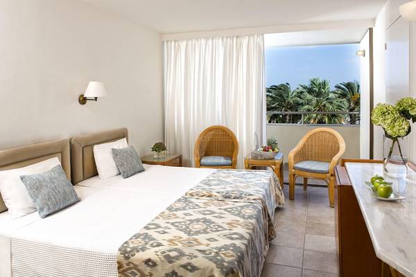 Doppelbettzimmer im Agapi Beach Resort Hotel mit Balkon und Ausblick auf Palmen.