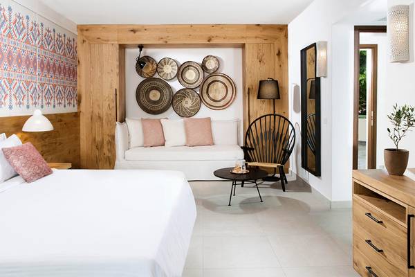 Innenansicht eines Zimmers im Agapi Beach Resort mit einem Bett, einer Couch, einem Tisch und dekorativen Elementen.