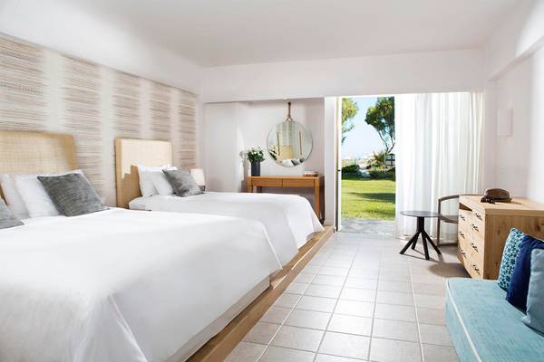 Innenansicht eines Doppelzimmers im Agapi Beach Resort mit zwei Betten, einem Tisch und einer Aussicht auf eine Wiese.