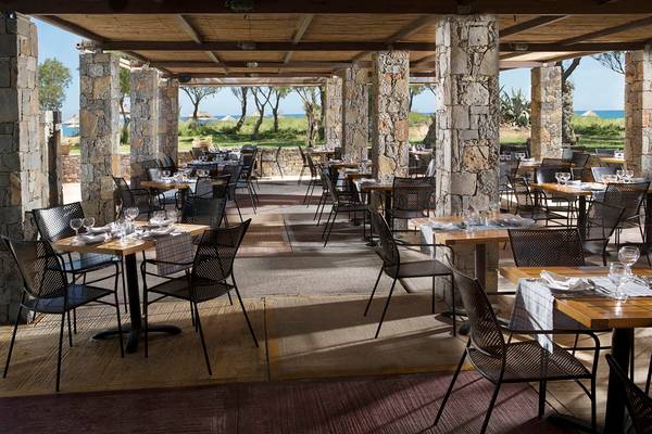 Restaurant des Agapi Beach Resorts mit Steinsaeulen und Tischen im Freien mit Blick auf das Meer