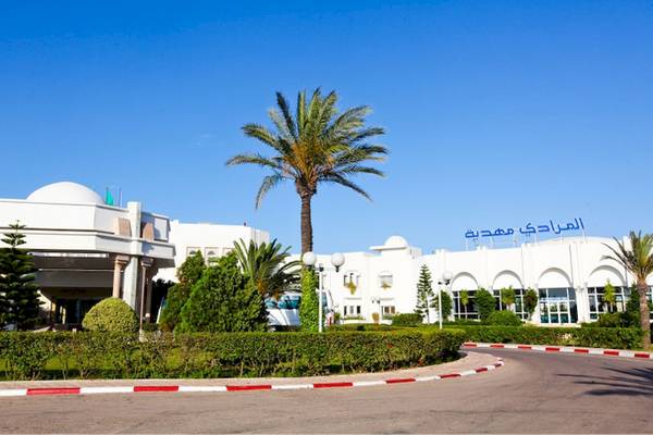 Außenansicht des El Mouradi Mahdia Hotels mit weißen Gebäuden, Palmen und Büschen