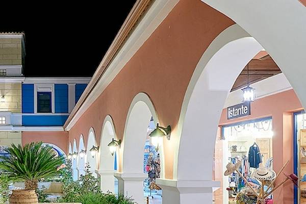 Außenansicht des Aldemar Olympian Village Hotels bei Nacht mit blauen und rosafarbenen Gebäuden und Pflanzen.