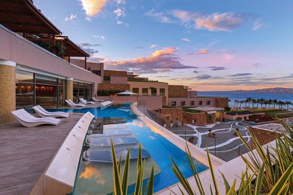 Außenpool des Miraggio Thermal Spa Resorts bei Sonnenuntergang mit Lounge-Liegestühlen und Blick auf das Meer.