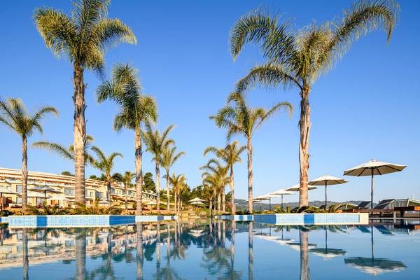 Außenpool des Miraggio Thermal Spa Resorts mit mehreren Palmen und Sonnenschirmen.