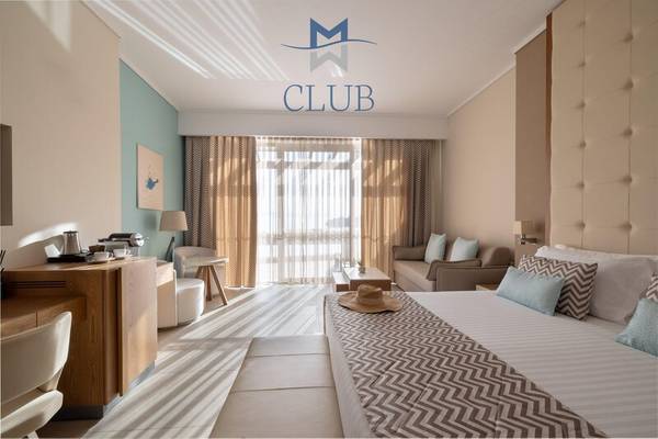 Innenansicht der Club Suite im Miraggio Thermal Spa Resort mit Bett, Wohnzimmerbereich und Logo.