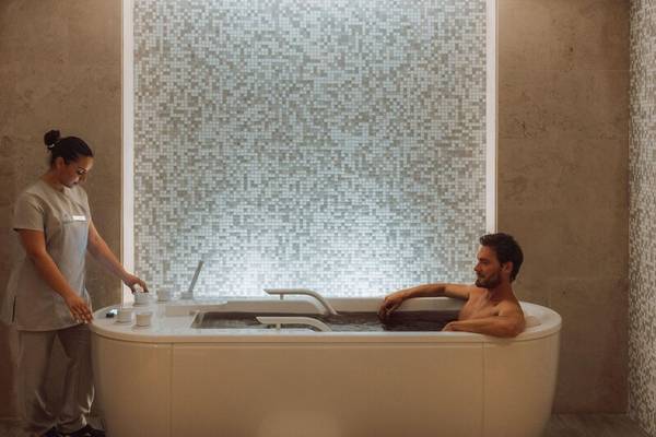 Ein Mann genießt eine entspannende Zeit in der Badewanne im Miraggio Thermal Spa Resort, während eine Frau ihm gegenübersteht.