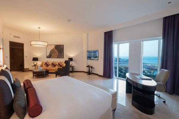 Innenansicht einer Suite im Rixos Marina Abu Dhabi mit Meerblick, einem großen Bett, Schreibtisch und Wohnzimmerbereich.