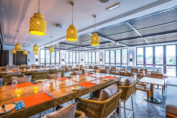 Restaurant im Rixos Marina Abu Dhabi mit vielen Tischen und Stühlen, gelben Lampen und großen Fenstern.
