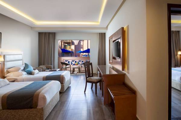 Innenansicht eines Hotelzimmers im Pickalbatros Aqua Park Resort in Hurghada mit drei Betten, Schreibtisch und Fernseher.