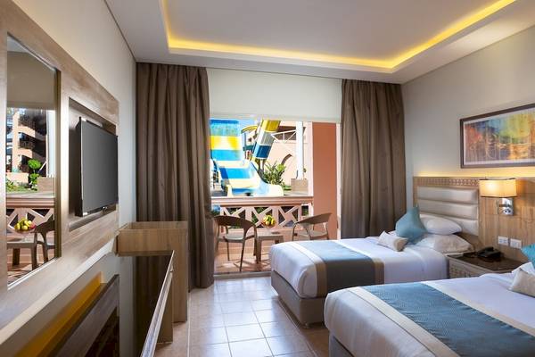 Doppelzimmer mit Balkon im Pickalbatros Aqua Park Resort - Hurghada, zeigt zwei Betten, Fernseher und einen Balkon mit Blick auf eine Wasserrutsche.