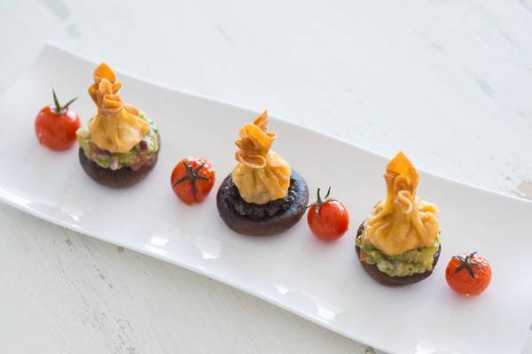 Fünf gebackene Champignons mit Avocadocreme und Tomaten auf weißem Teller