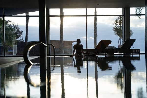 Frau sitzt im Pool im Baia Azul Hotel, mit großen Fenstern und Ausblick auf die Landschaft.