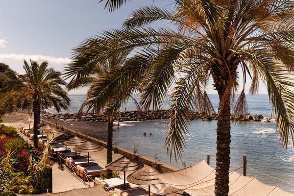 Blick auf den Strand des Saccharum Hotels mit Palmen und Sonnenschirmen.