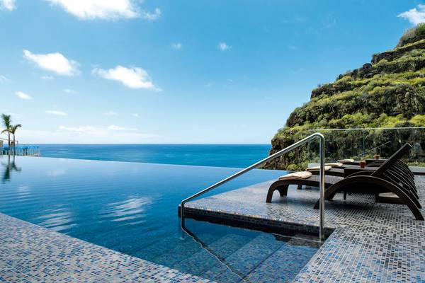 Infinity-Pool am Rand des Felsens im Saccharum Hotel mit Loungeliegen und Blick auf den Ozean.