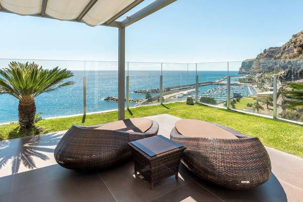 Terrasse mit zwei großen Korbsofas und einem kleinen Tisch, mit Aussicht auf das Meer und einen Hafen.
