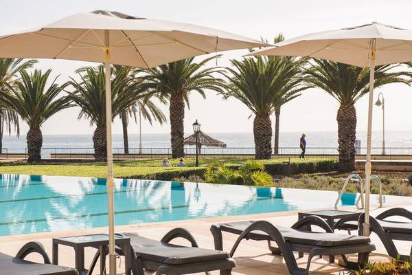 Außenpool des Vila Galé Santa Cruz mit Liegestühlen, Sonnenschirmen und Palmen am Meer