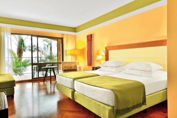 Doppelzimmer im Pestana Promenade Hotel mit zwei Betten, gelben Kissen und einem Ausblick auf eine Terrasse.