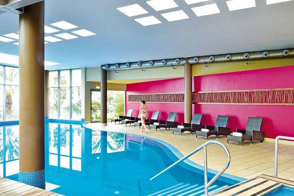 Poolbereich im Pestana Promenade Hotel mit Frau, Lounge-Sesseln und magentafarbenen Wänden.