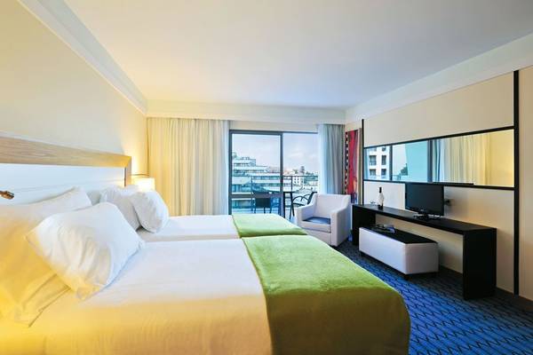 Zwei Betten mit weißem und grünem Überwurf in einem Hotelzimmer mit Stadtblick.