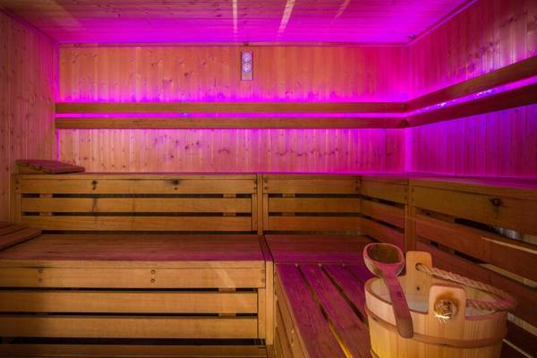 Eine Sauna mit Holzbänken und rosa Beleuchtung, ein Eimer mit einem Holzlöffel daneben.