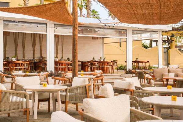 Außenbereich des Calheta Beach Hotel mit vielen Tischen und Stühlen unter einem Sonnendach.