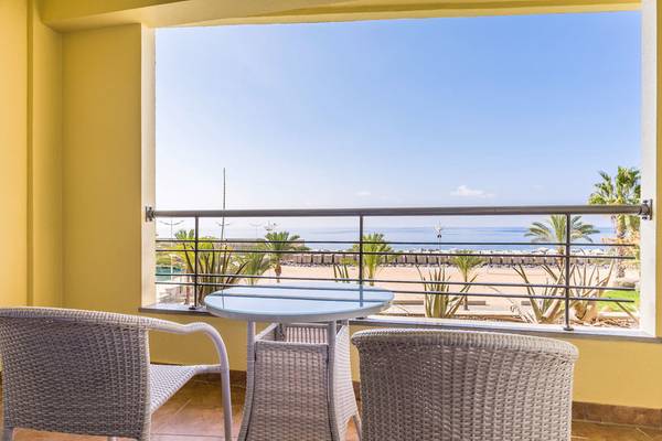 Ausblick auf das Meer vom Balkon des Calheta Beach Hotels mit zwei Rattanstühlen und einem Tisch.