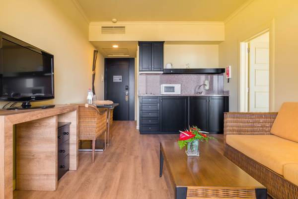 Suite im Calheta Beach Hotel mit Fernseher, Esstisch, Sessel, Sofa und Küchenzeile.