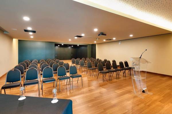 Konferenzraum im Views Baia Hotel mit blauen Stühlen, Glastischen und einem Rednerpult.