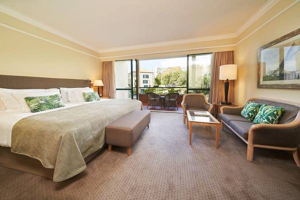 Hotelzimmer im Cliff Bay mit großem Bett, Wohnzimmerbereich und Balkon.