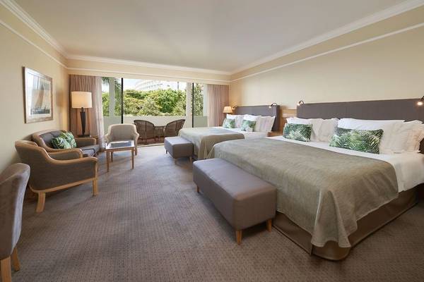 Hotelzimmer mit zwei Betten und Sitzmöbeln, Blick auf Außenterrasse und Bäume