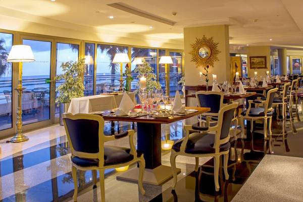 Innenansicht des Restaurants im Royal Savoy Hotel mit gedeckten Tischen und Meeresblick.