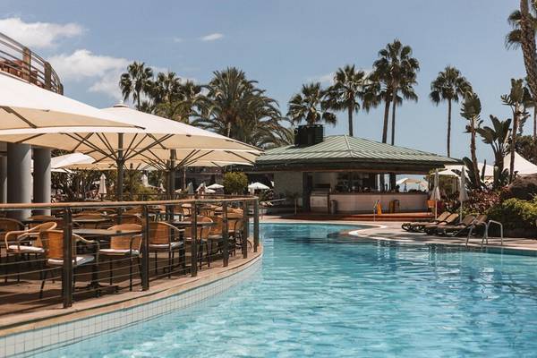 Außenbereich des Royal Savoy Hotels mit Swimmingpool, Sonnenliegen und Sonnenschirmen.