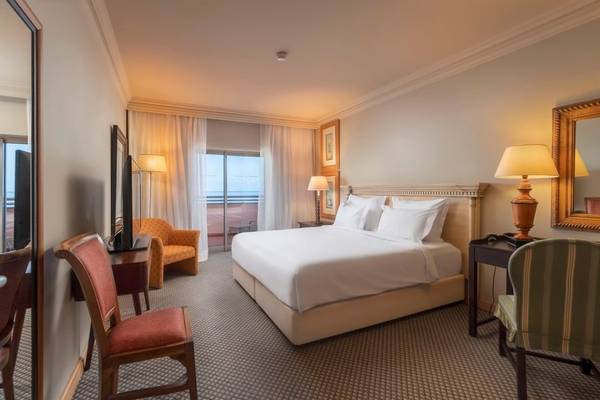 Innenansicht eines Hotelzimmers im Royal Savoy mit großem Bett, Schreibtisch und Aussicht auf den Ozean.
