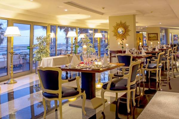 Innenansicht des Restaurants im Royal Savoy Hotel mit gedeckten Tischen und Blick auf das Meer.