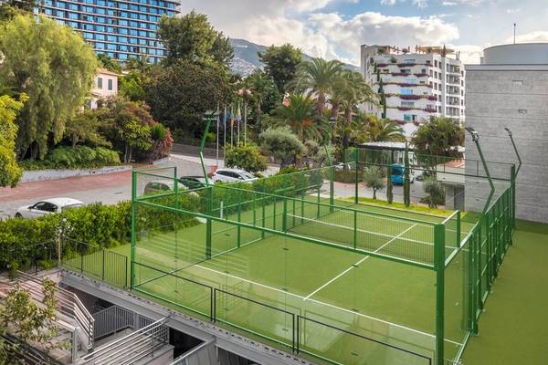 Tennisplatz auf der Terrasse des Royal Savoy Hotels, umgeben von Bäumen und Gebäuden.