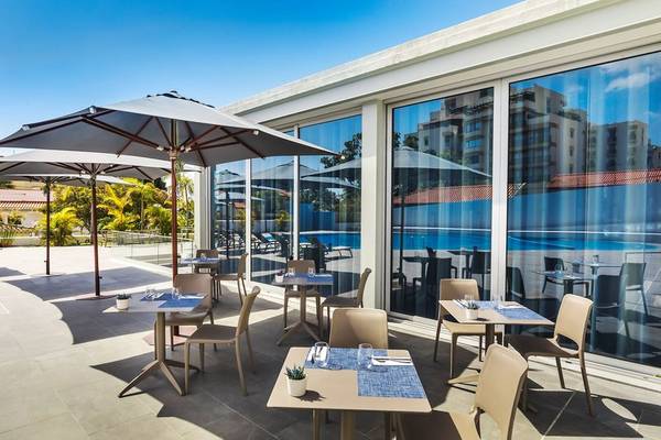 Terrasse des Allegro Madeira Hotels mit Tischen, Stühlen und Sonnenschirmen, Blick auf den Pool.