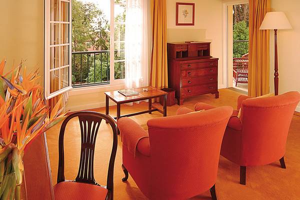 Hotelzimmer mit Balkon und Sitzecke, zwei rote Sessel, Tisch, Blumen und Lampe.