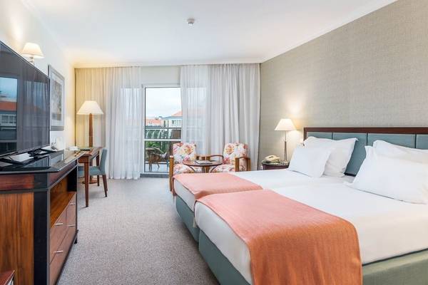 Hotelzimmer im Pestana Grand Premium Ocean Resort mit zwei Betten, Fernseher, Schreibtisch und Balkon.