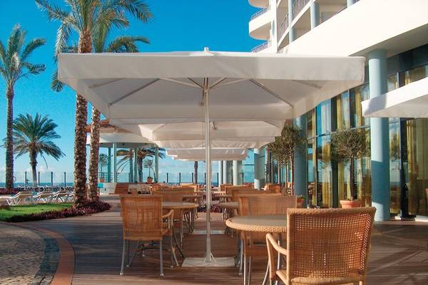 Terrasse des Pestana Grand Premium Ocean Resort mit Tischen und Stühlen unter weißen Sonnenschirmen.