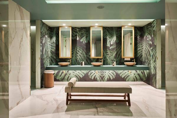 Badezimmer im Savoy Palace mit tropischen Tapeten, drei Waschbecken und Spiegeln, einer Bank und Marmorböden.
