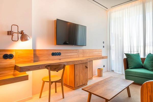 Innenansicht eines Hotelzimmers im 3HB Faro mit Schreibtisch, Fernseher, Wandlampe und grünem Sofa.