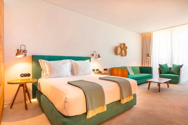 Hotelzimmer im 3HB Faro mit grünen Möbeln, weißem Bett, Tisch, Sofa und Lampen.