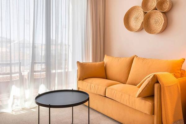 Wohnzimmer im 3HB Faro mit einem gelben Sofa, einem schwarzen Tisch und einer weißen Vorhang vor einem Balkon.